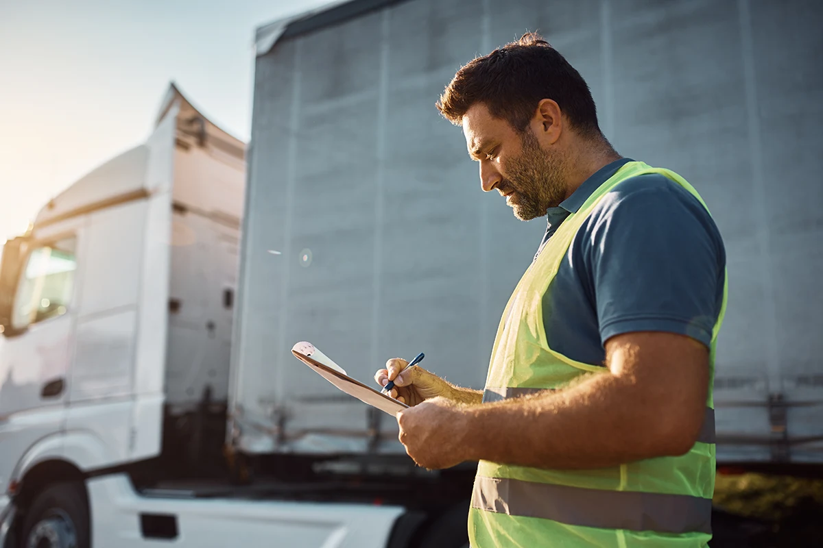 Spediteur macht Notizen auf Klemmbrett vor LKW.